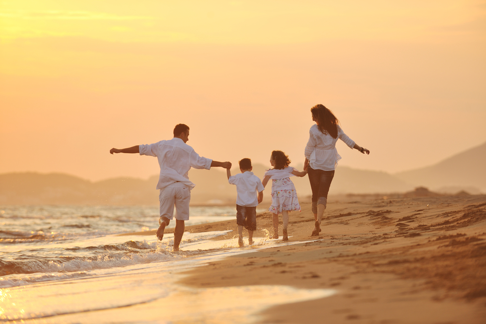 happy young family have fun on beach run and jump  at sunset